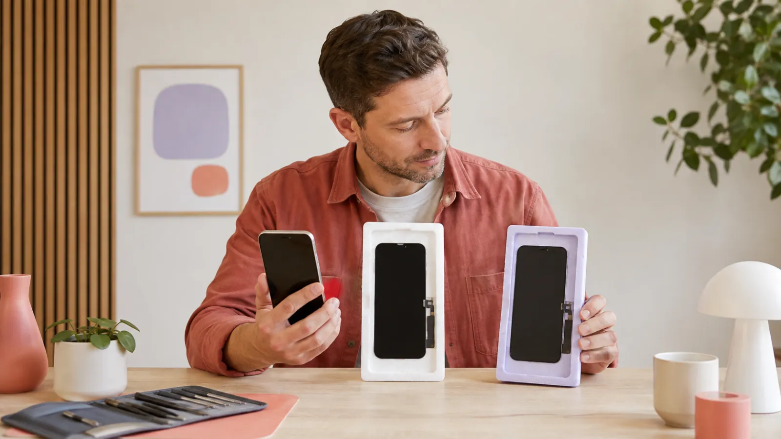 Man jämför två olika ersättningsskärmar med sin iPhone på ett reparationsbord